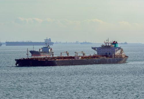 Laden crude oil tanker underway along vessels anchored on outer anchorage in Singapore Strait.