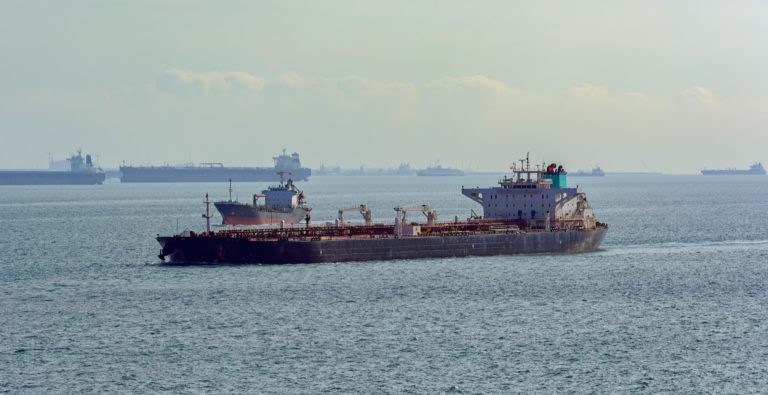 Laden crude oil tanker underway along vessels anchored on outer anchorage in Singapore Strait.
