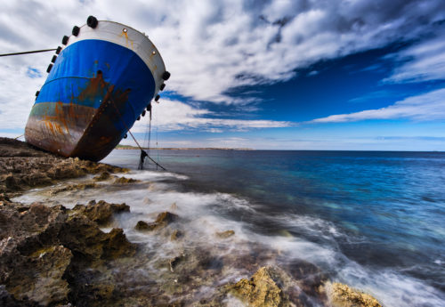 Sea view to stranded ship on the shore of Buggiba, Malta. Anchor placed on the shore. Shipwreck accident on rough stones shore.