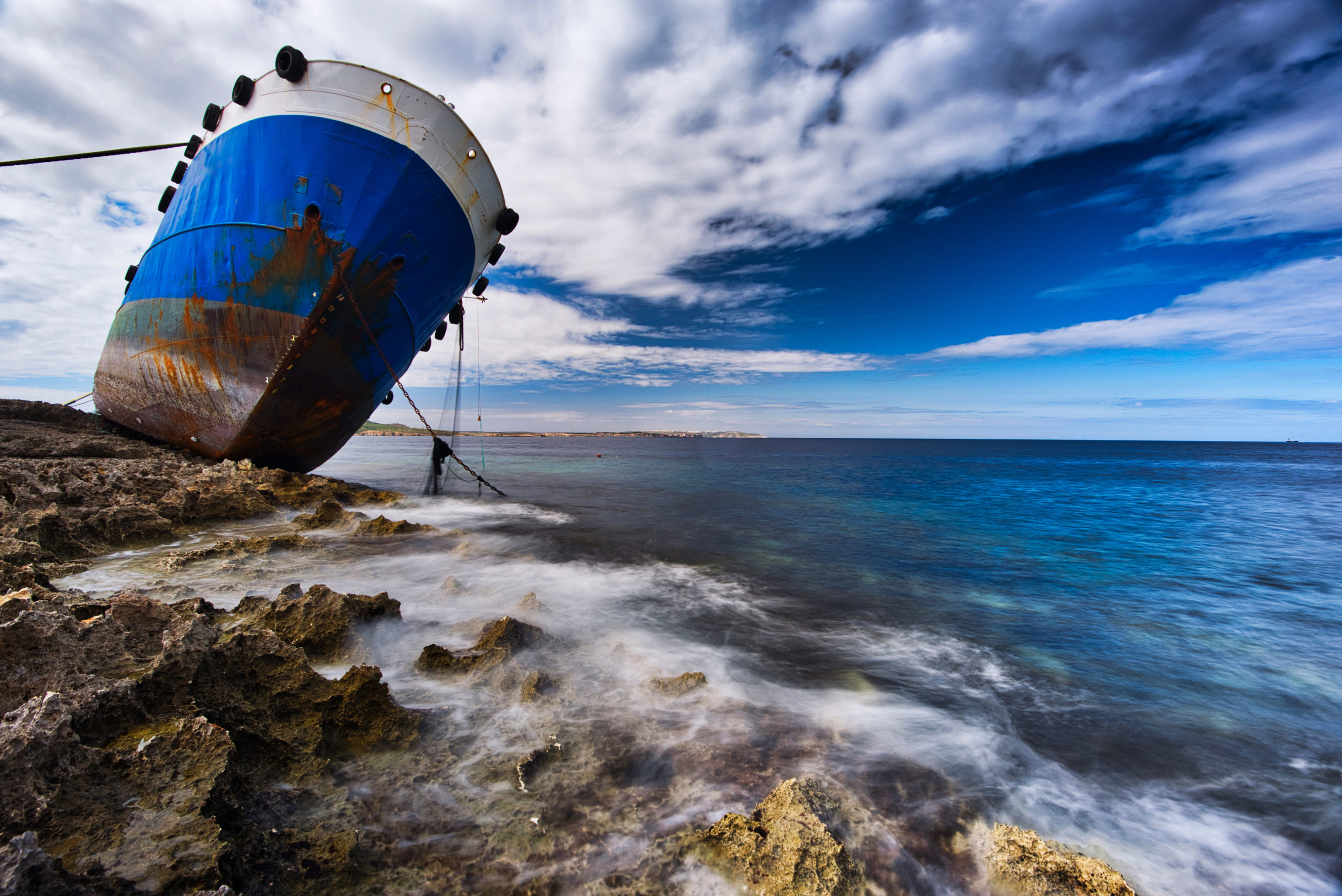 Sea view to stranded ship on the shore of Buggiba, Malta. Anchor placed on the shore. Shipwreck accident on rough stones shore.