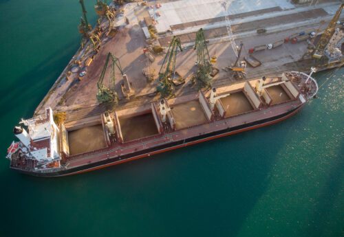 Aerial top view of big cargo ship bulk carrier is loaded with grain of wheat in port at sunset