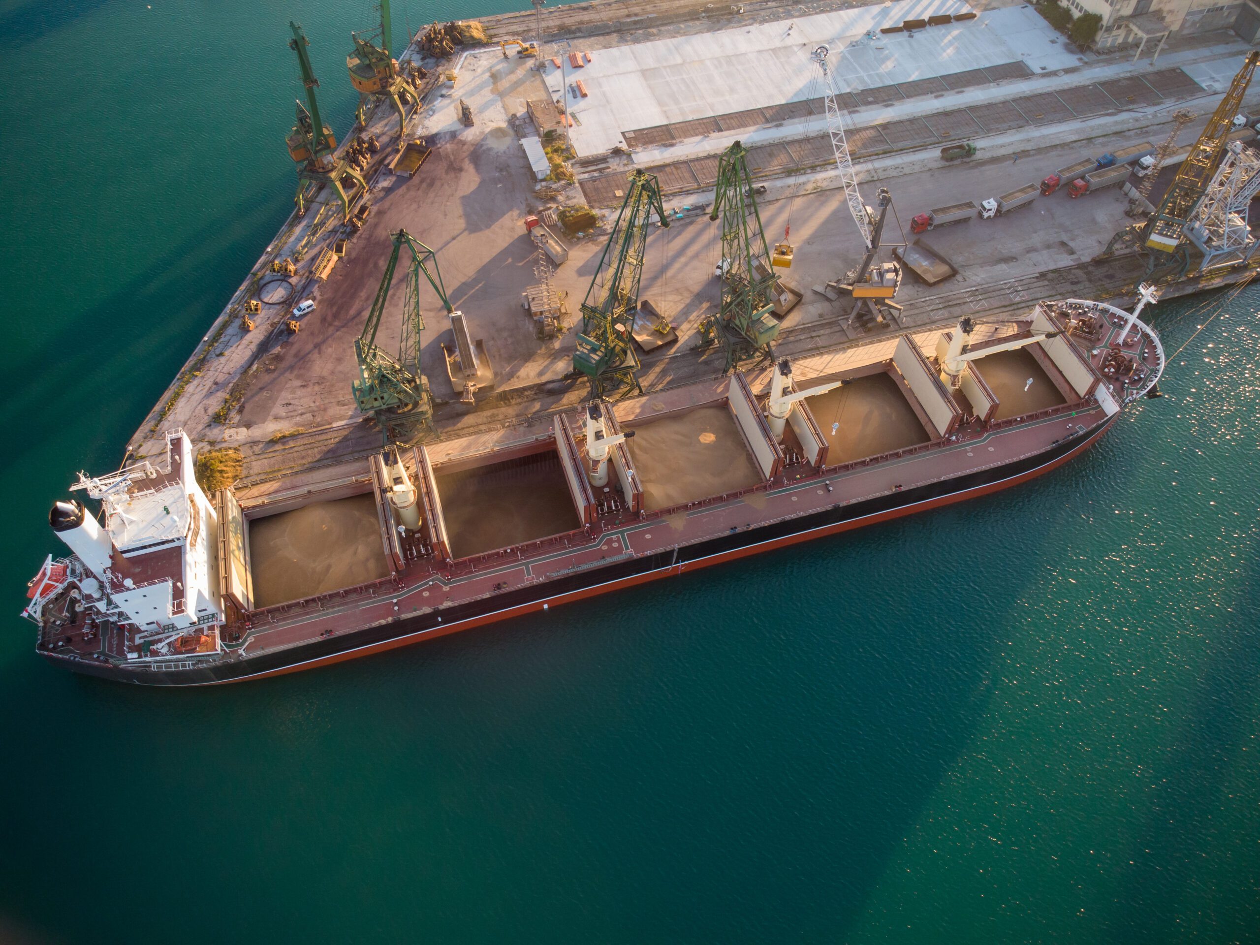Aerial top view of big cargo ship bulk carrier is loaded with grain of wheat in port at sunset