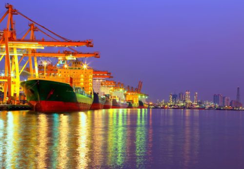 Industrial Container Cargo freight ship with working crane bridge in shipyard at dusk for Logistic Import Export with oil plant background