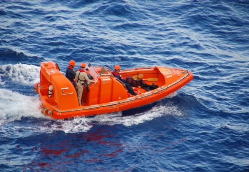 Training exercise to rescue man overboard in bright orange rescue boat.