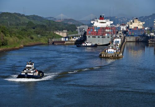 Container ships and a tug boat at the Miraflores Locks at the Panama Canal, linking the Atlantic and Pacific Oceans, and a major tourist destination.