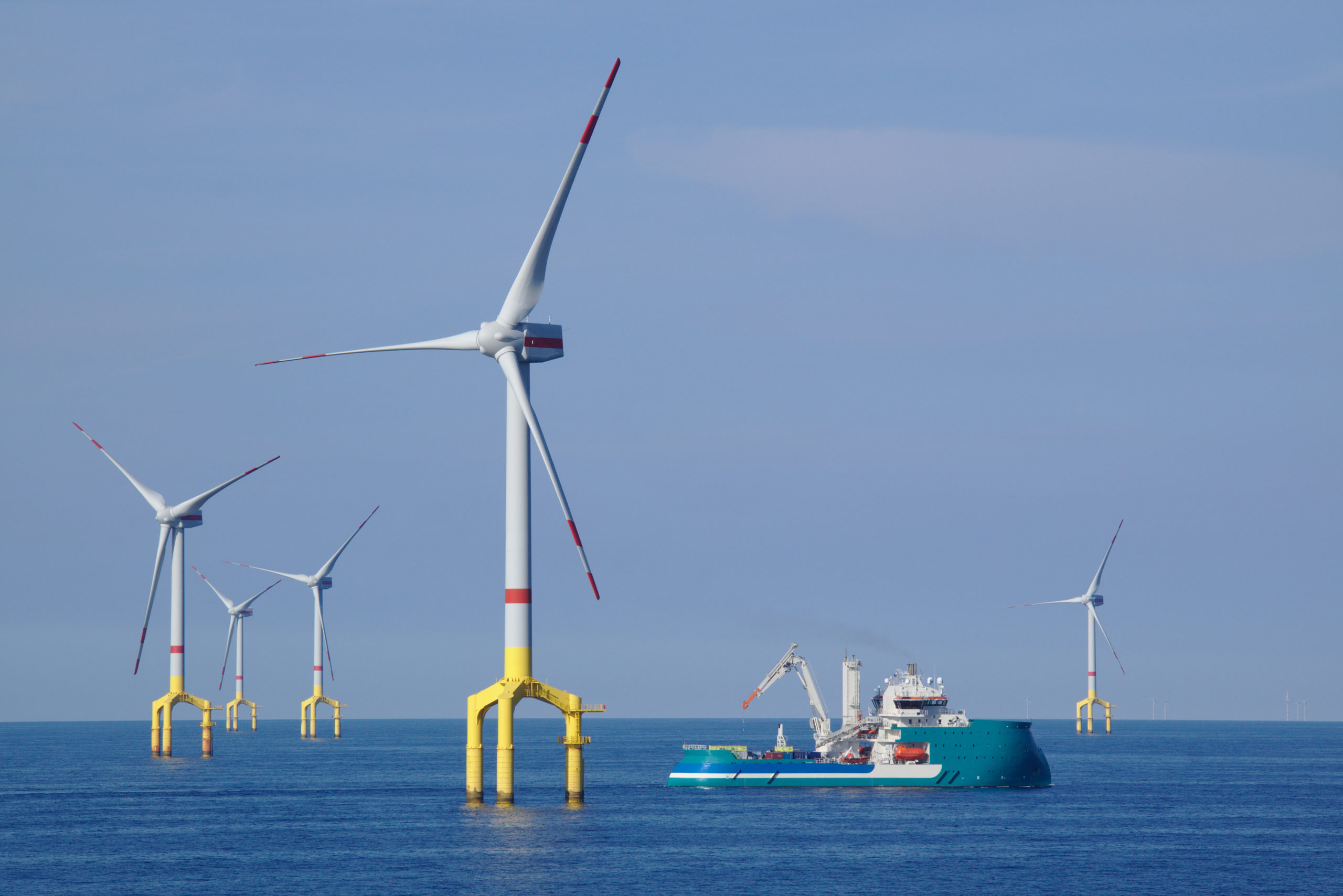 Offshore wind turbine with supply boat in the north sea with blue sky and sea