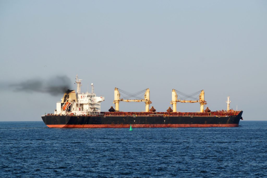 Cargo ship with black smoke from the chimney on the sea horizon.