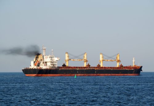 Cargo ship with black smoke from the chimney on the sea horizon.
