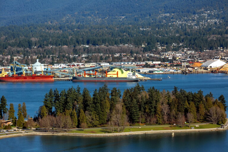 Terminal of North Vancouver port on a background of mountain scenery. The vessel is under load, and a tug is towing another vessel.