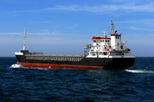 Small coastal cargo ship of about 4000 dwt underway at sea in calm weather over blue sky.