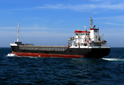 Small coastal cargo ship of about 4000 dwt underway at sea in calm weather over blue sky.