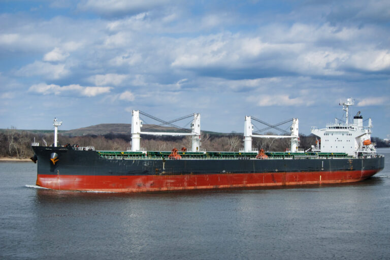 Empty Supramax bulk carrier with deck cranes sailing on a river calm water
