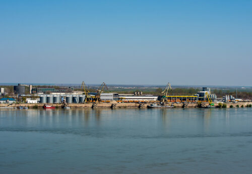 Danube river port with ships, silos, lifting cranes, tanks, warehouses and industrial buildings.
