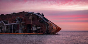 Sunrise time photo of rusty wreaked ship on the purple sea surface