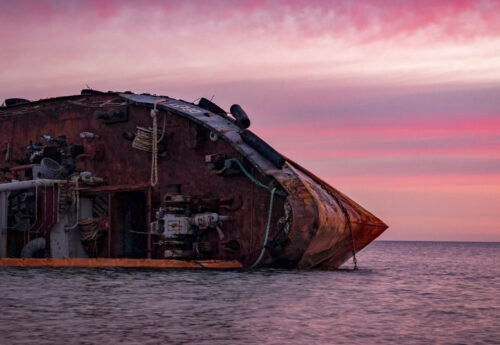 Sunrise time photo of rusty wreaked ship on the purple sea surface