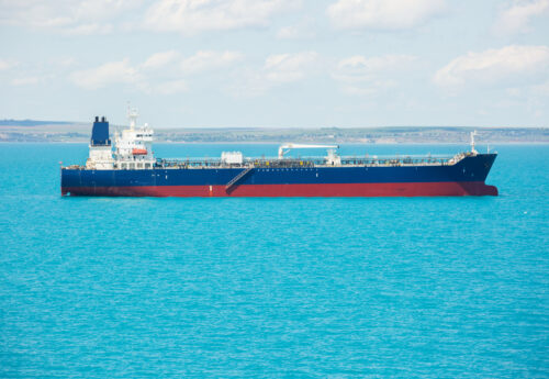 Red and blue oil product tanker at anchorage of a port.