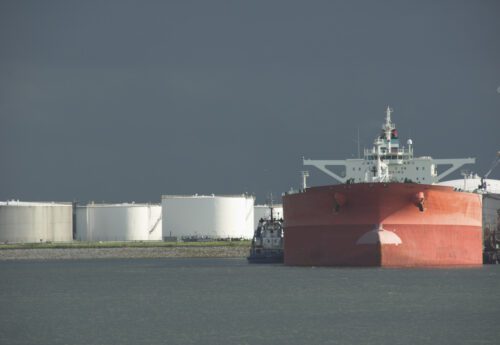 Product oil tanker in harbour with storage tanks.