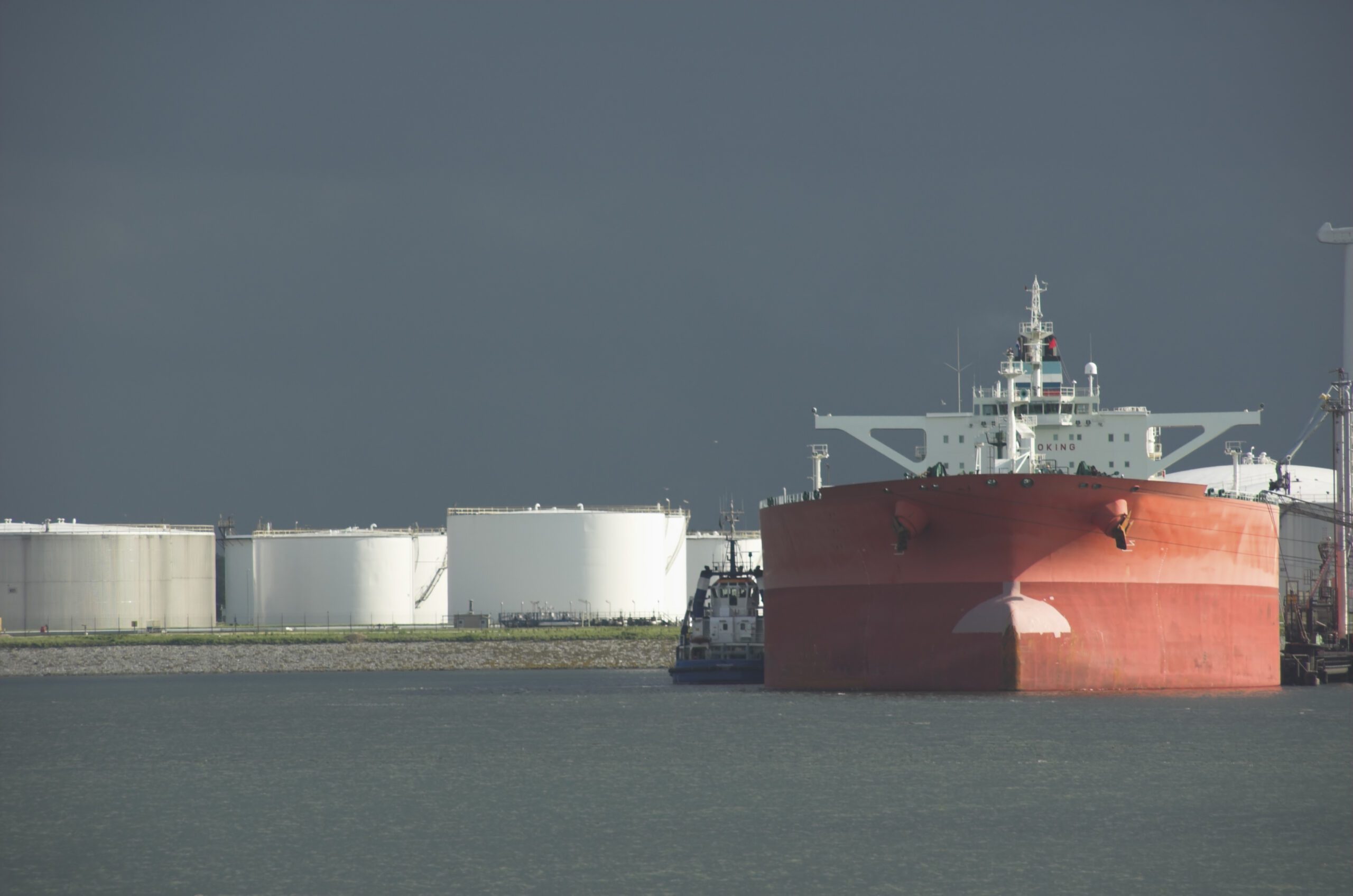Product oil tanker in harbour with storage tanks.
