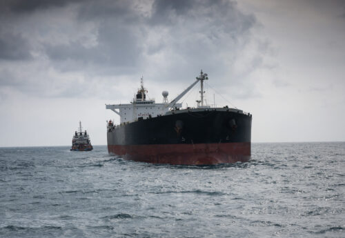 Crude oil tanker at open sea with tugboat tied up at astern